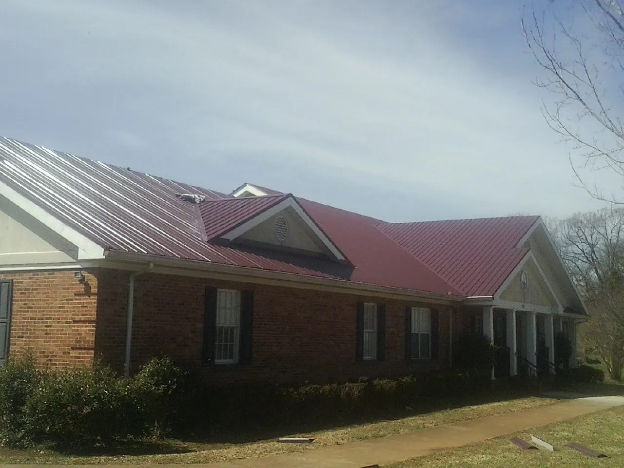 Red metal roof with gabled entries on a long brick building, from a Hail Damage Roof Repair job in Lake Waccamaw
