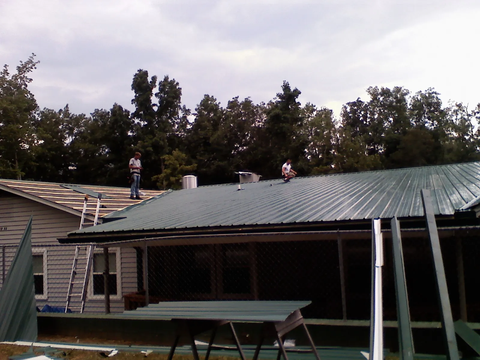 Two roofers installing green metal panels above a covered porch in Lake Waccamaw