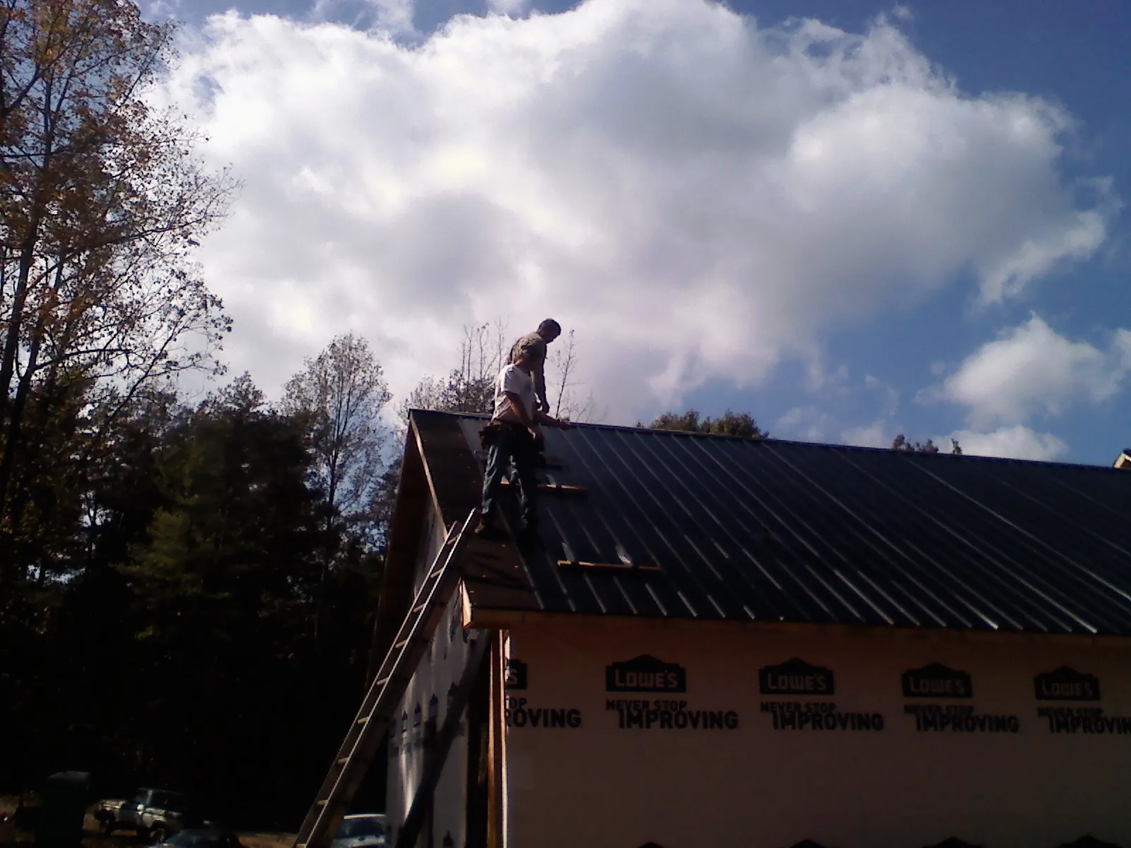 Roofer fastening dark metal panels high against a cloudy sky, from a Roof Inspection job in Lake Waccamaw