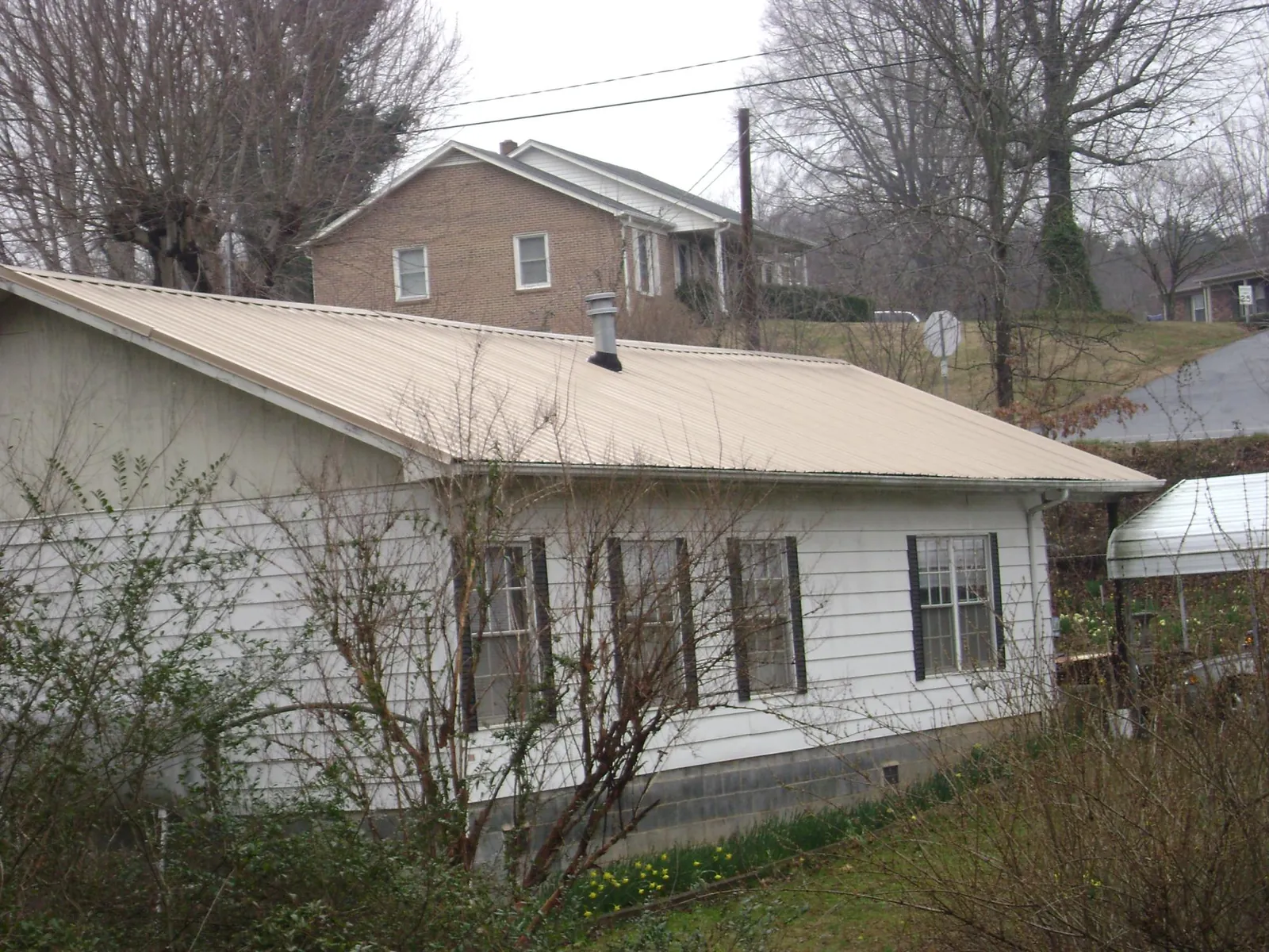 Tan metal roof on a white sided house set into a hillside — Commercial Roofing by Roofing Brothers in Lake Waccamaw